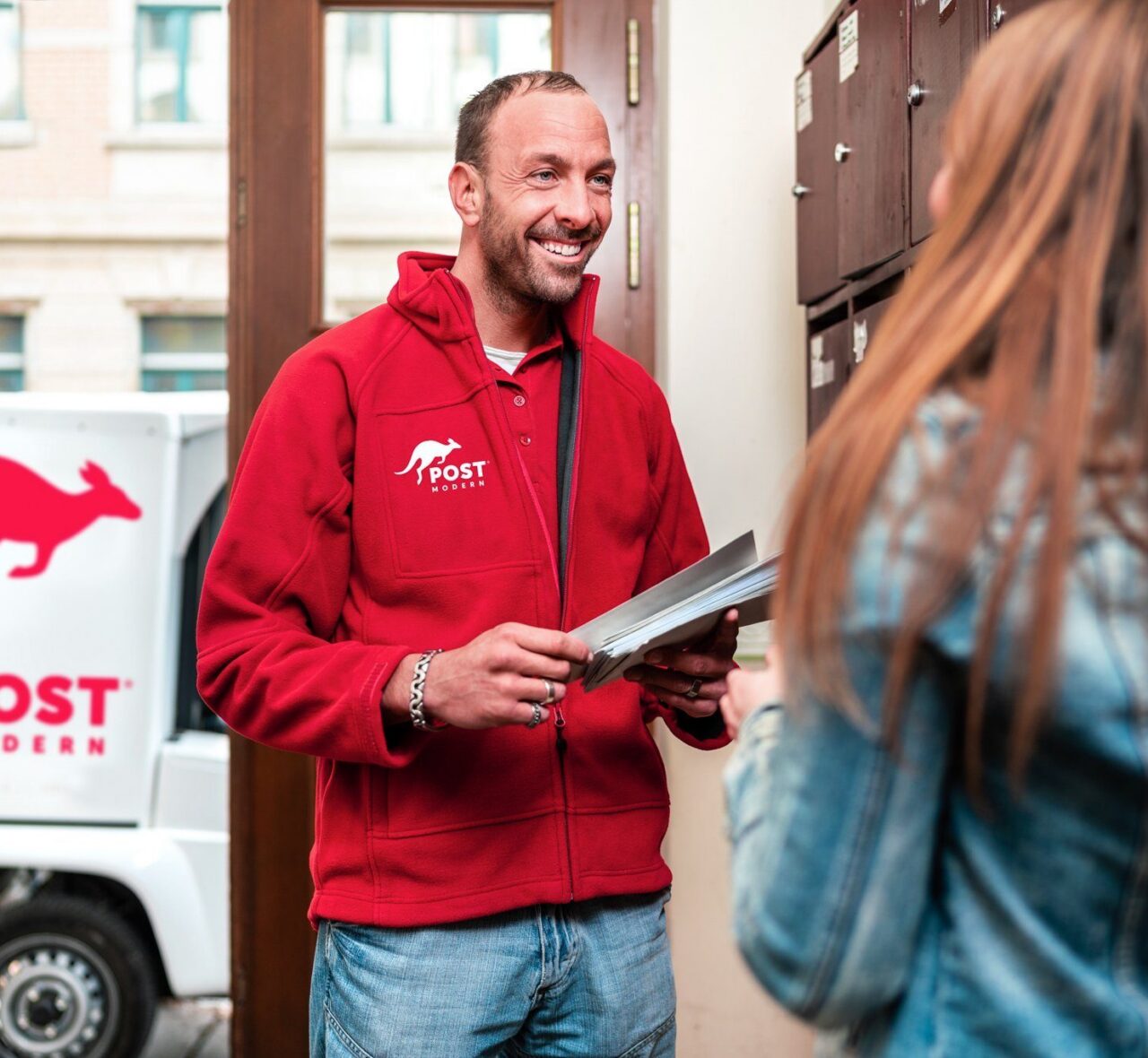 Das Bild zeigt einen PostModern-Zusteller, welcher gerade die Briefe persönlich zustellt.