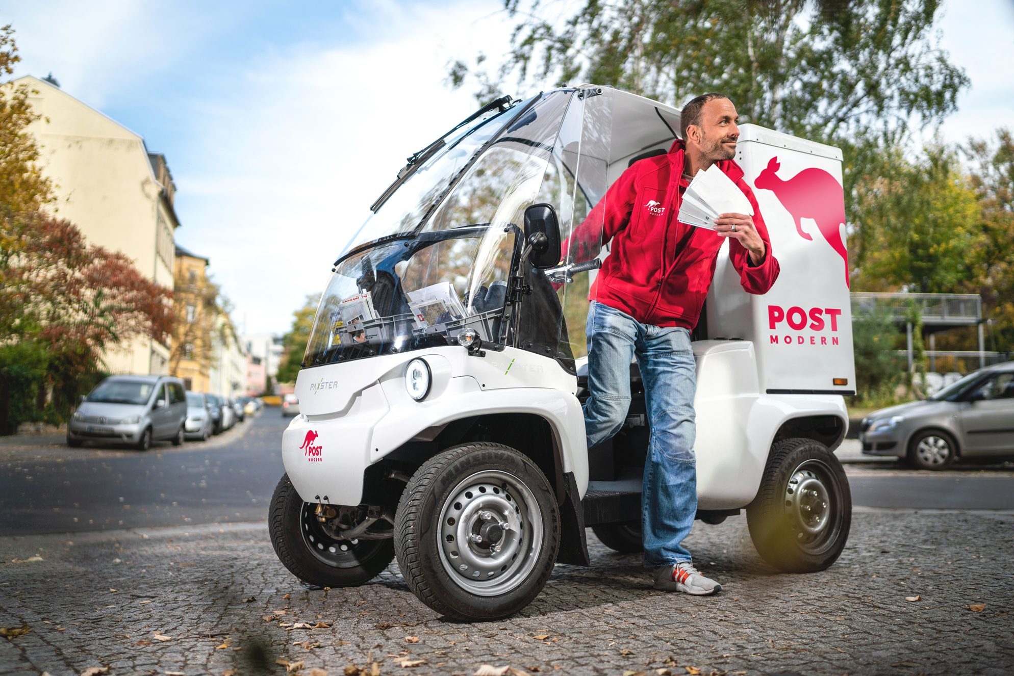 Das Bild zeigt einen Mitarbeiter von PostModern, welcher mit Briefen aus einem Paxster von PostModern steigt.